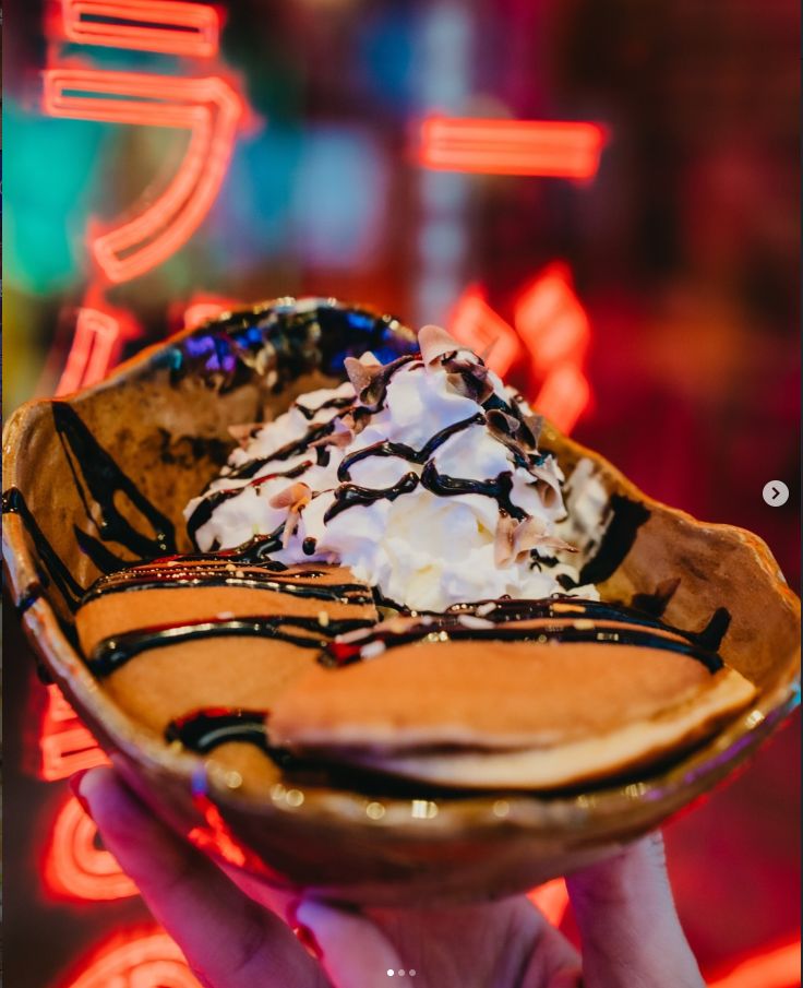 Postre con helado, chocolate y nata sobre el neón del local