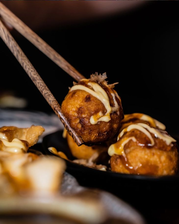 Unos palillos cogiendo una bola frita con salsa okonomiyaki y mayonesa